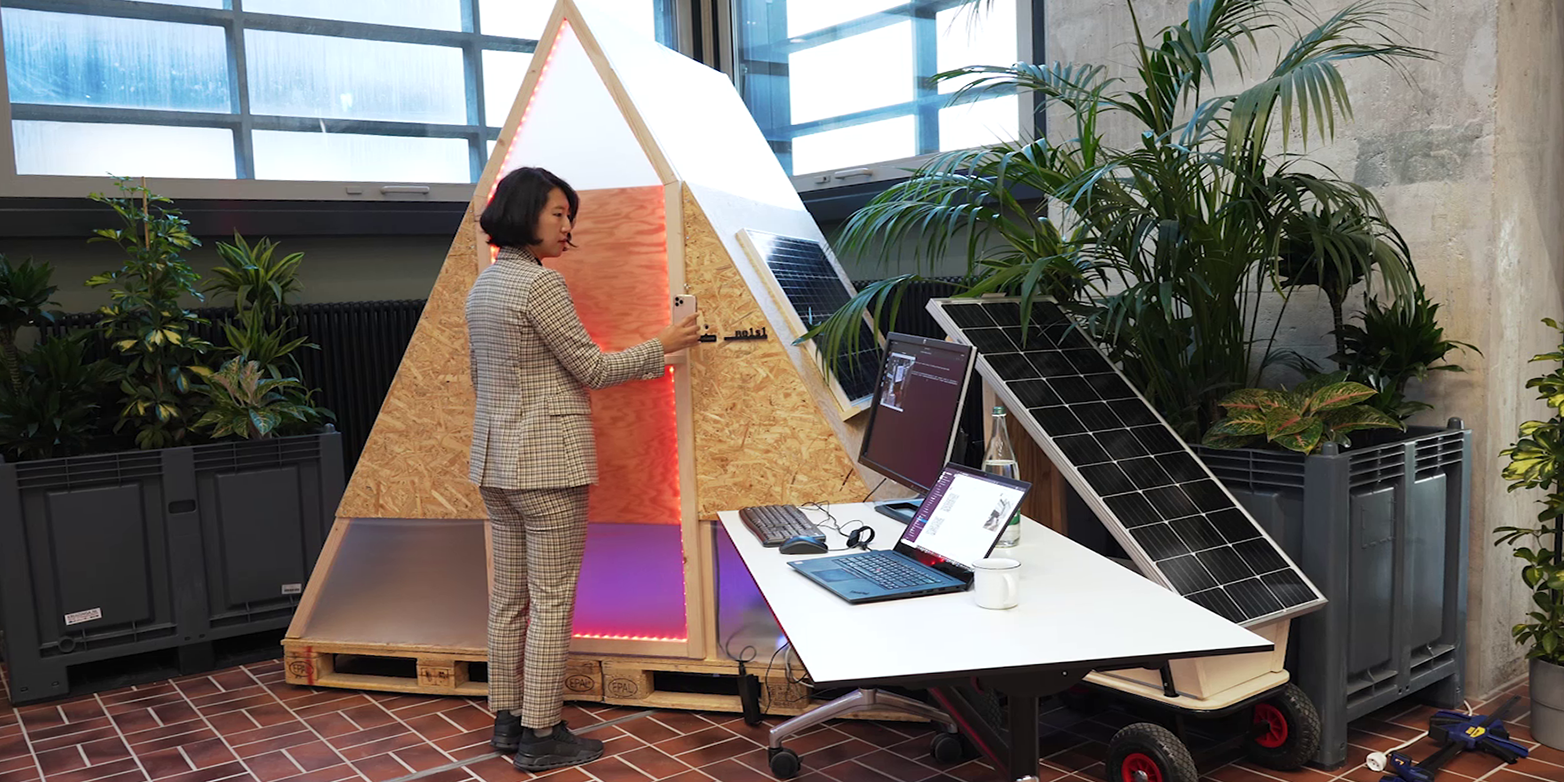 Eine Frau steht vor einem dreieckigen Kasten mit Laptop und Solarpanel