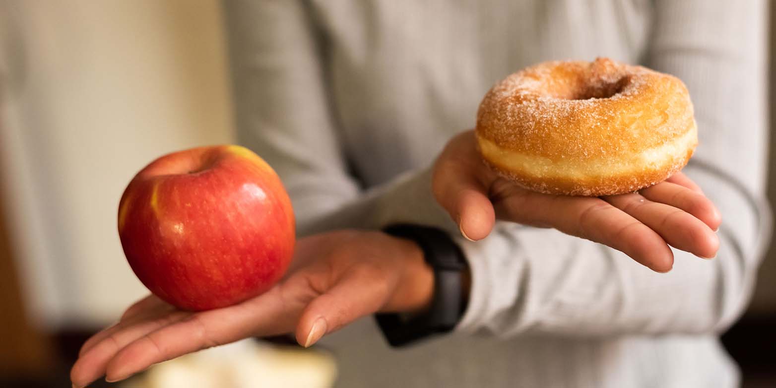 Zwei Hände halten einen Apfel (links) und einen Donut (rechts)