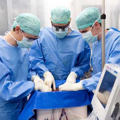 3 Chirurg:innen beugen sich über die Perfusionsmaschine