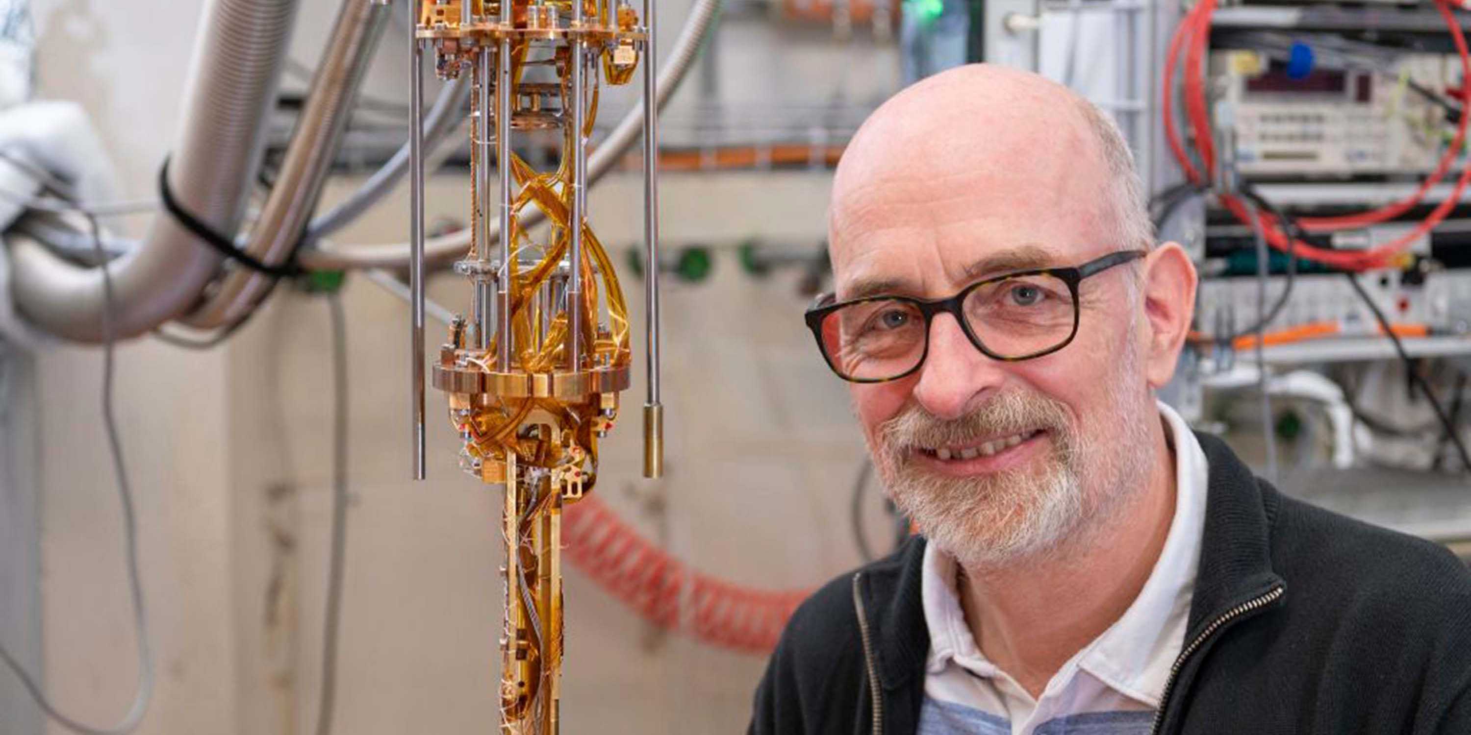 Klaus Ensslin steht lächelnd vor einem Quantencomputer