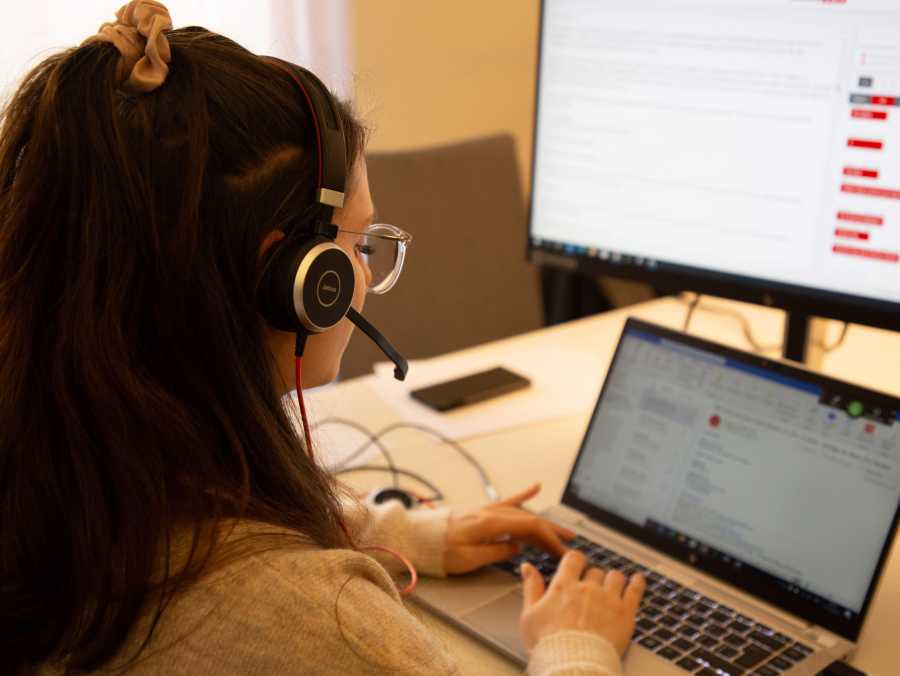 Schriftdolmetscherin beim Tippen auf einem Laptop. Vor ihr ein Zweitbildschirm mit abgebildeter Chatfunktion fr das Schriftdolmetschen.