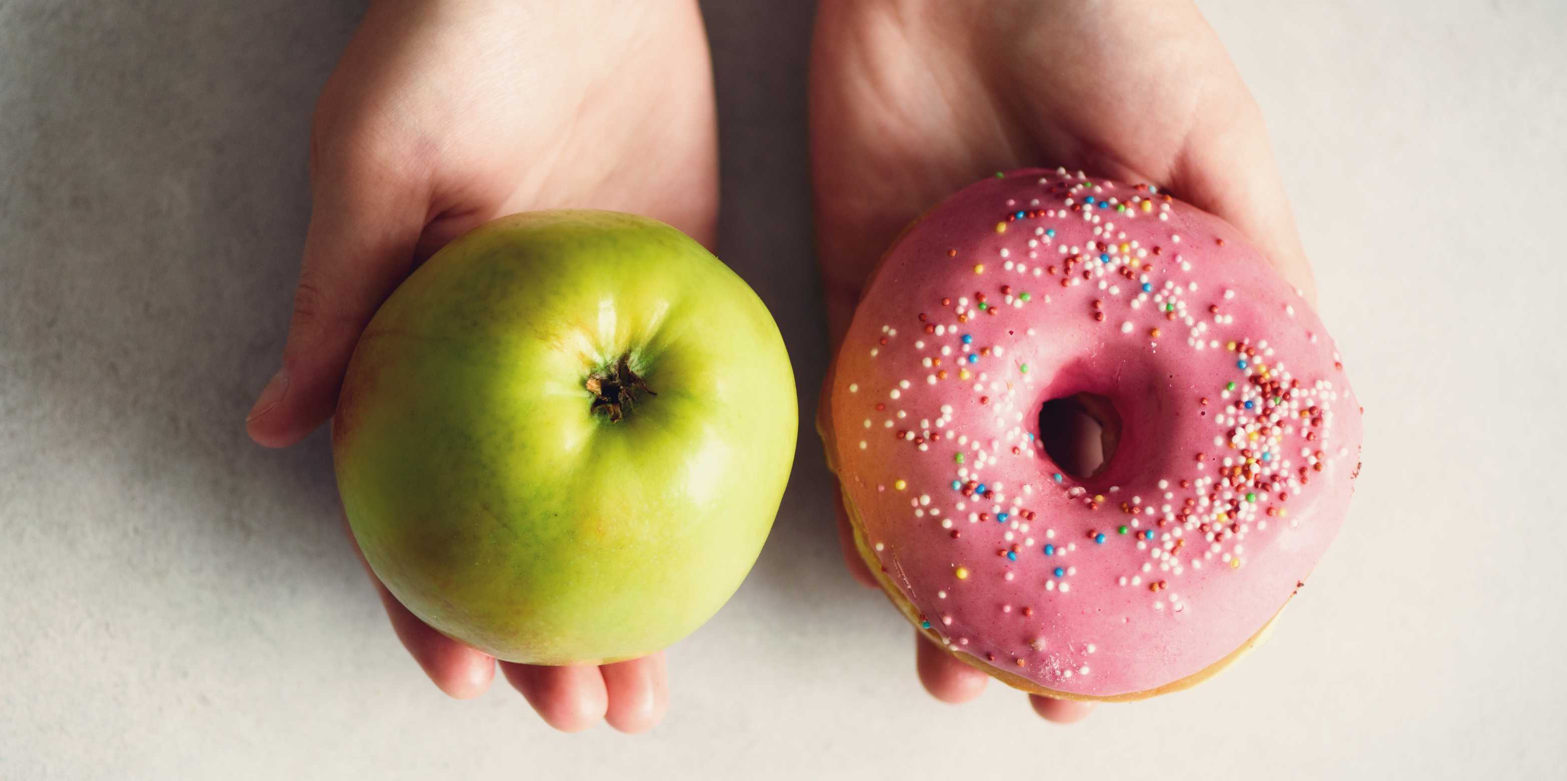 Eine Person präsentiert auf der einen Hand einen Apfel, auf der anderen einen Donut.
