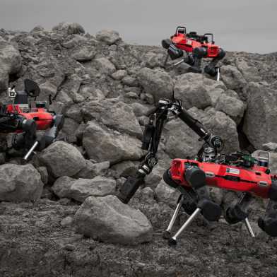 Drei Laufroboter (rot) in einer steinigen Landschaft (Kiesgrube).