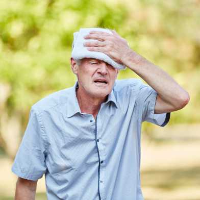 Ein alter Man hält sich ein feuchtes Tuch auf die Stirn und verzieht leidend das Gesicht.