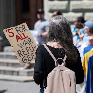 Eine Frau hält ein Schild in der Hand auf dem steht 'S' FOR ALL WAR REFUGEES