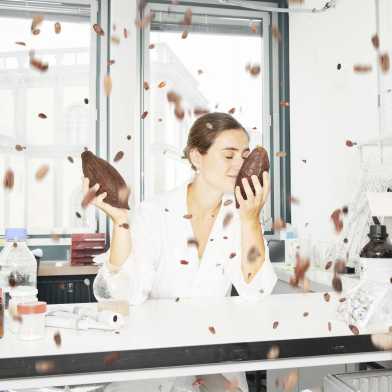 Frau sitzt in einem Labor und riecht an einer Kakao-Bohne